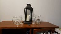 Luminara lantern and nine clear glass vases arranged on wood surface