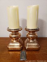 Front view of both mercury glass candle holders with lit cream-colored flameless LED candles and remote control placed in front.