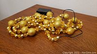 Gold bead garland with integrated yellow lights on a table surface.