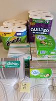 Overview of the full lot showing Bounty paper towels, Quilted Northern toilet paper pack, Kleenex hand towels, and multiple Puffs Plus Lotion tissue boxes.