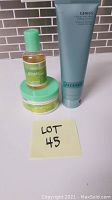 Algenist Genius Ultimate Melting Cleanser tube with Arbonne Ginger Citrus body wash and cream, arranged on a white surface with tile background.