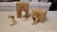 Three Willow Tree figurines displayed together with two original boxes visible behind them, shown on a white surface