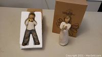 Two Willow Tree figurines shown outside of packaging on a table, Heart of Gold (boy) and Angel of Hope (angel) in front of original boxes
