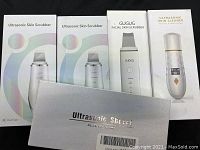 Five boxed ultrasonic skin scrubbers including two HailiCare, one GUGUG, one with digital display, and one in silver box