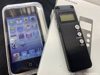 Apple iPod touch inside clear plastic case beside a small black audio player on top of a white box showing the front of both devices