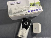 Video doorbell unit, doorbell chime, and original packaging box displayed on a gray surface.