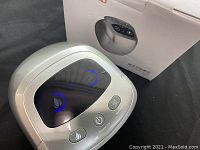 Front view of knee massager with power, heat, and vibration buttons and original box shown behind.