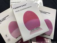 Six boxed pink silicone facial cleansing brushes including one visible in plastic clamshell packaging showing detail of bristles and control buttons