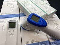 Close up of Kaiyi infrared thermometer with blue detail, resting on packaging box and manuals.