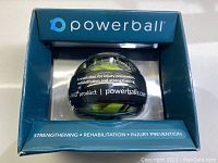 Front view of Powerball gyroscope in original packaging showing branding and basic product information about injury prevention, rehabilitation, and strengthening.