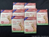 Photo of 8 boxes of SOFT Touch Foot Peel Mask, stacked in two rows of four each, showing front packaging with product name, product benefits, and image of legs.