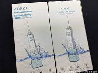 Two boxed AIMO portable oral irrigators show packaging design with water splash graphics, device buttons and branding.