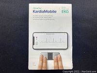 Box showing AliveCor KardiaMobile branding and image of device used with smartphone app displaying EKG graph.