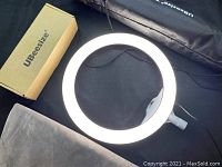 Photo of a glowing UBeesize LED ring light with attached power cable and black fabric carrying bag, next to a UBeesize branded cardboard box.