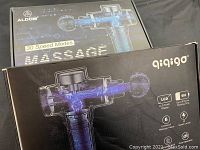 Three boxed massage guns by Aldom, Qiqigo, and Hoposo showing packaging and branding.