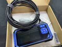 Endoscope device with display and long coiled flexible cable placed inside a foam-lined cardboard box.