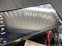 Front angled view showing touchscreen with volume and function buttons on the side, device placed on black surface with cables partially visible.