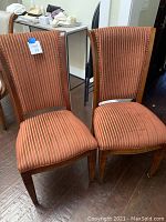 Two matching wood frame dining chairs with red and beige vertical striped fabric upholstery on seats and backs. Chairs show signs of use and wear on fabric.