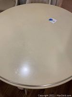 Close-up of round table top showing cream color surface with some marks and a metal edging around the rim.