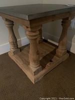 Wooden side table with turned legs and dark stone top seen from an angle showing the legs and base.