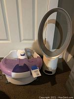 Full view of white and purple Conair foot bath with attachments next to white bladeless oscillating fan on floor.