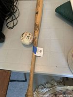 Photo showing the wood baseball bat laying flat with the baseball beside it on a light-colored table.