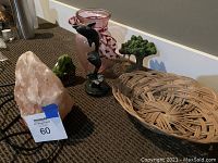 Photo showing pink crystal salt lamp, black marble dolphin statue, green bonsai tree sculpture, pink glass vase with ribbon, and round wicker basket on brown surface.