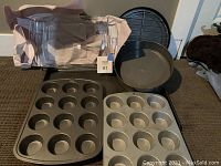 Photo showing two metal muffin tins, one non-stick black cake pan, one metal pizza/cake pan, and one Pyrex glass baking dish wrapped in paper.