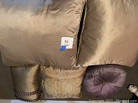 Photo showing assorted pillows in beige and lavender tones, includes large square pillows, bolster, embroidered and round pillows