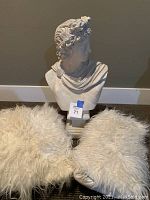 Two beige fuzzy pillows with a white classical bust sculpture behind them on the floor.
