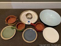 Overview of all eight items arranged on carpet showing various stoneware plates, two soup bowls, and chip and dip plate.