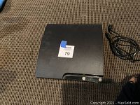 Top view of the black PS3 console with sticker showing lot number, placed on carpeted surface.