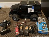 Side view of the black remote control Hummer vehicle with large off-road tires, remote controller, multiple rechargeable battery packs and charger on carpeted floor.