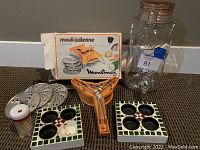 Full view of kitchen mandoline, multiple metal slicing discs, ceramic candle holders, plastic water jug and vegetable string cutter