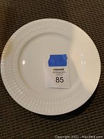 Full view of one white dinner plate with a dotted decorative rim and a MaxSold tag number 85.