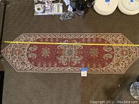 Full view of the rectangular handcrafted table runner with pointed ends, lying flat showing the entire pattern and design on a carpeted floor.