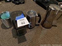 Lot includes a coffee grinder, creamer cup, and stovetop coffee maker on a carpeted floor.