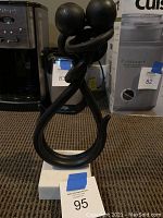 Pewter sculpture of two abstract embracing figures, black in color, standing on a small white base, photo taken from the front.