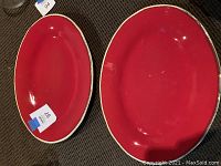 Two large oval red serving platters with cream/beige edges shown side by side to display matching design and size.