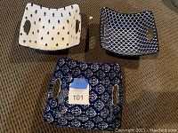 Three square ceramic serving bowls with handles, distinct blue and white decorative patterns, arranged on carpeted floor.