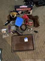 Wide view of all items in the lot laid out on a carpet, including the Monopoly game box, serving tray, scarf, mask, belts, grooming tools, and other small household items.