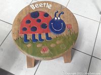 Top view of round wooden stool seat with carved and painted ladybug (beetle) design and the word 'Beetle' painted above it.