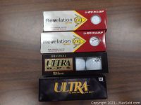Four sleeves of new golf balls including Dunlop Revelation and Wilson Ultra shown on wood surface.