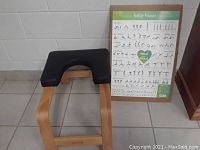 FeetUp Trainer yoga inversion stool with wooden base and black padded cushion next to an instructional poster.