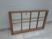 Full view of rectangular wooden frame mirror with 8 glass panes, laid on floor against wall