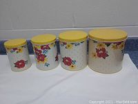 All 4 sizes of nested floral canisters with yellow lids displayed in a row