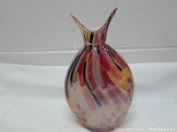 Full view of the tall multi-coloured glass vase with striped pattern and unique flared double-spout top, standing on a white fabric background.