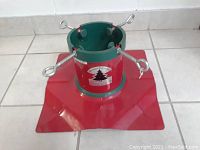 Full view of the bright red and green metal Christmas tree holder with four adjustable screws for securing the tree.