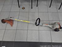 Full view of the 58-inch Stihl weedeater lying on tiled floor showing entire shaft, cutting guard, and engine handle area.