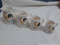 Front view of all four vintage ceramic measuring cups with rooster design, showing size and color detail.